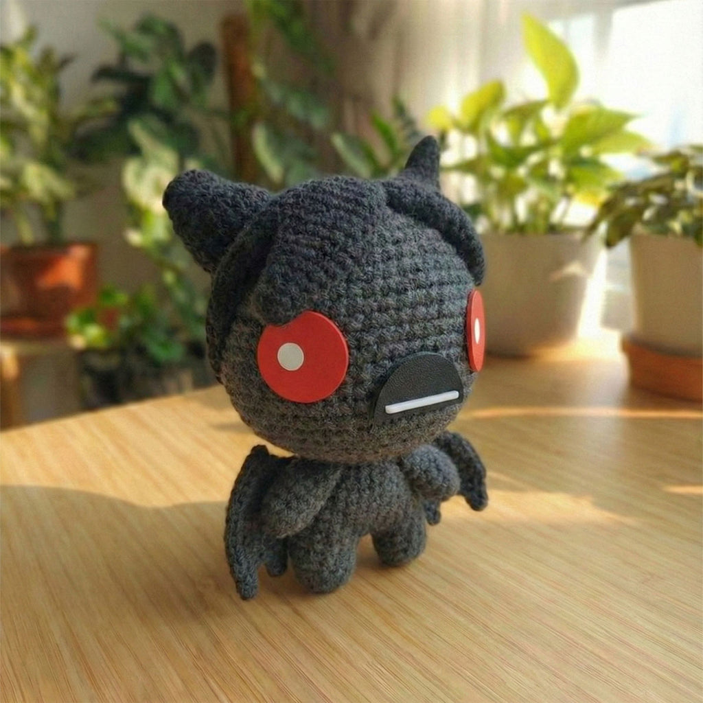 Amigurumi fatto a mano di Azazel dal videogioco The Binding of Isaac, realizzato all'uncinetto in grigio scuro e nero con ali da pipistrello e grandi occhi rossi circolari.