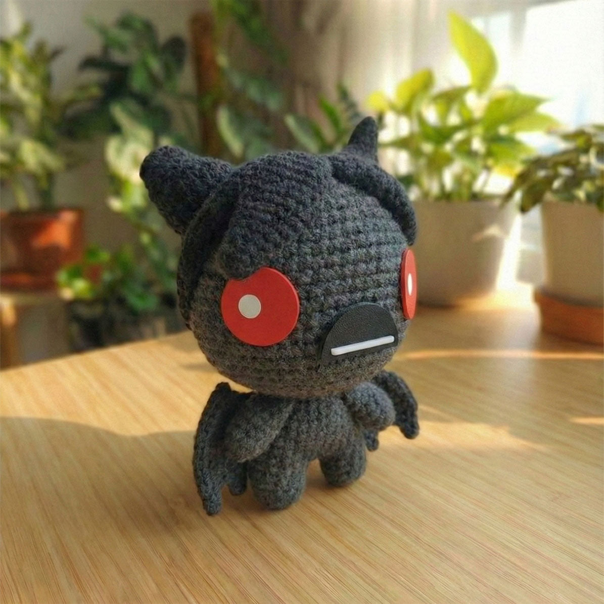 Amigurumi fatto a mano di Azazel dal videogioco The Binding of Isaac, realizzato all'uncinetto in grigio scuro e nero con ali da pipistrello e grandi occhi rossi circolari.